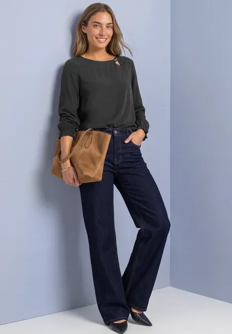 Blouse met ronde hals en gespdetail armor grey Een glimlachende vrouw in zwarte trui, wijde jeans en bruine clutch voor een lichte achtergrond.