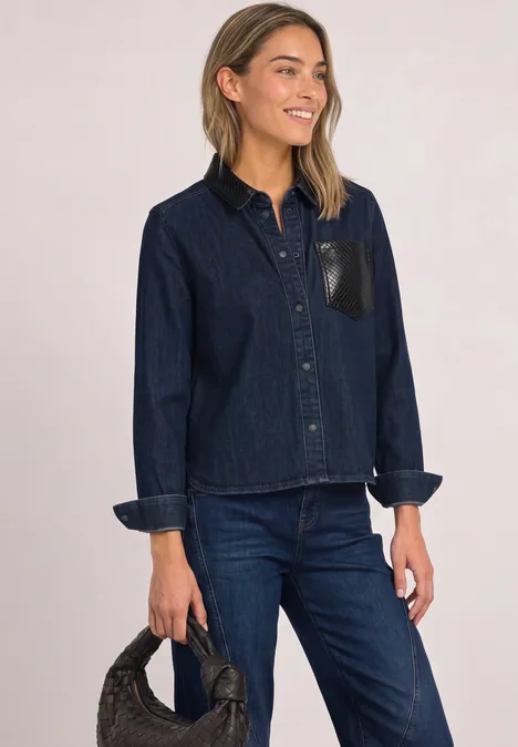 Frau in dunkelblauer Jeansjacke und Hose, hält schwarze Handtasche.
