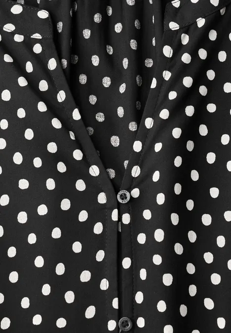 Schwarzes Kleidungsstück mit weißen Polka-Dots und V-Ausschnitt, vorn mit Knopfverschluss.