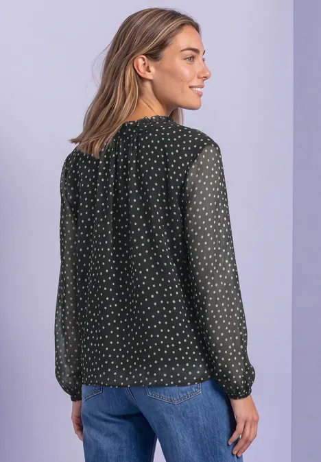 Vrouw in zwarte blouse met witte stippen en blauwe jeans, van achter gezien voor een tweekleurige paarse achtergrond.