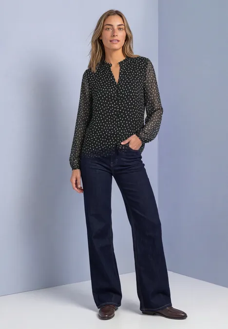 Vrouw in zwart, gestippeld shirt en wijde, donkere jeans voor paarse achtergrond.
