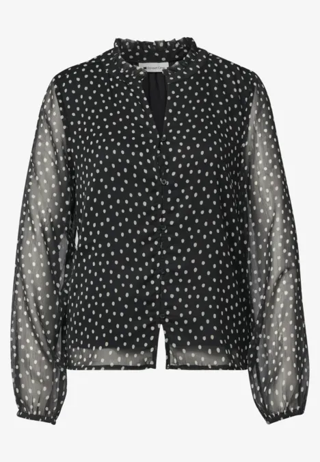 Zwarte transparante blouse met witte stippen, ruches aan de kraag en lange mouwen.