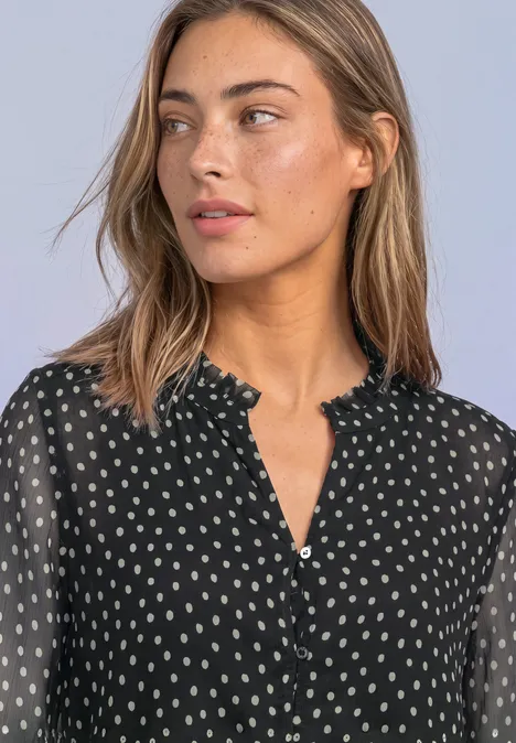 Jonge vrouw in zwarte, gestippelde chiffonblouse met gerimpelde kraag en doorzichtige mouwen.