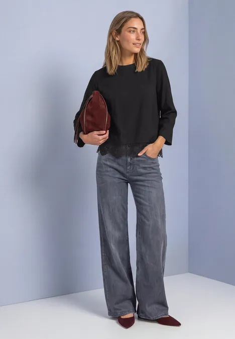 Frau trägt schwarze Bluse, weite graue Jeans, weinrote Tasche und spitze Schuhe.