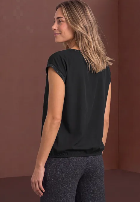 Sportieve vrouw in zwart T-shirt en grijze legging, rugaanzicht tegen een bruine achtergrond.