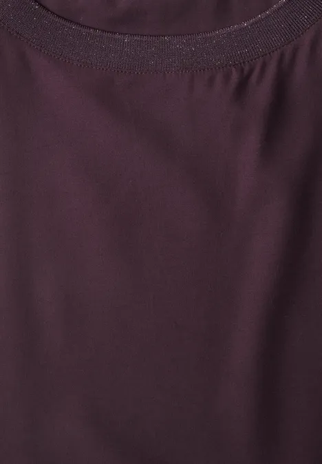 Gros plan sur l’encolure d’un t-shirt couleur baie, en tissu fin légèrement brillant.