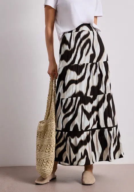 Wit shirt, lange rok met zwart-witte zebraprint, strozak en platte schoenen.