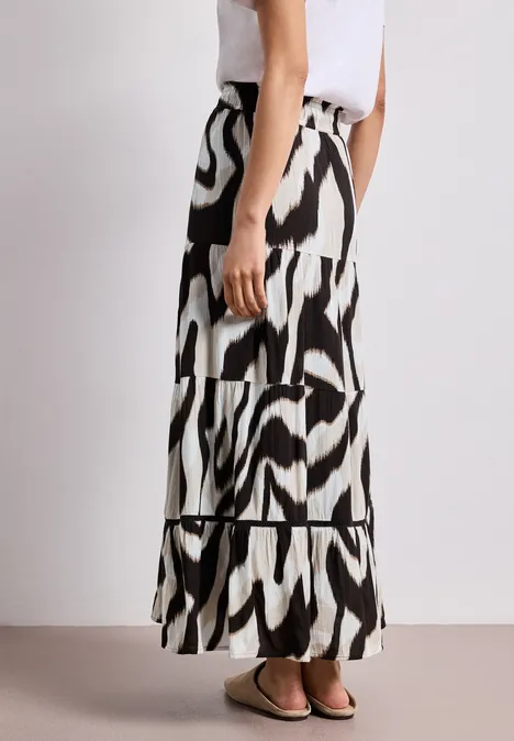 Zijaanzicht van een vrouw in een wit topje en lange zwart-witte zebrarok, gecombineerd met platte sandalen.