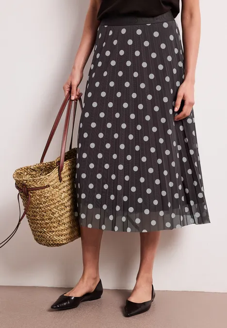 Zwarte midirok met witte stippen, zwarte ballerina’s en een gevlochten rieten tas.