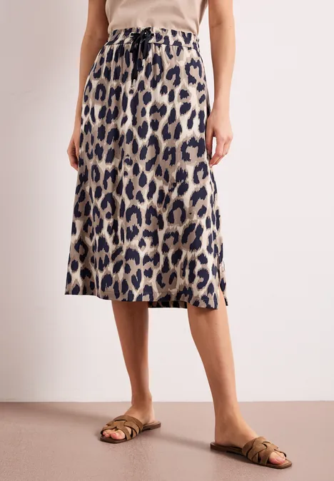 Midirock für Damen mit cremefarbenem Grund, schwarzem Leopardenmuster und elastischem Bund, dazu Riemchensandalen.