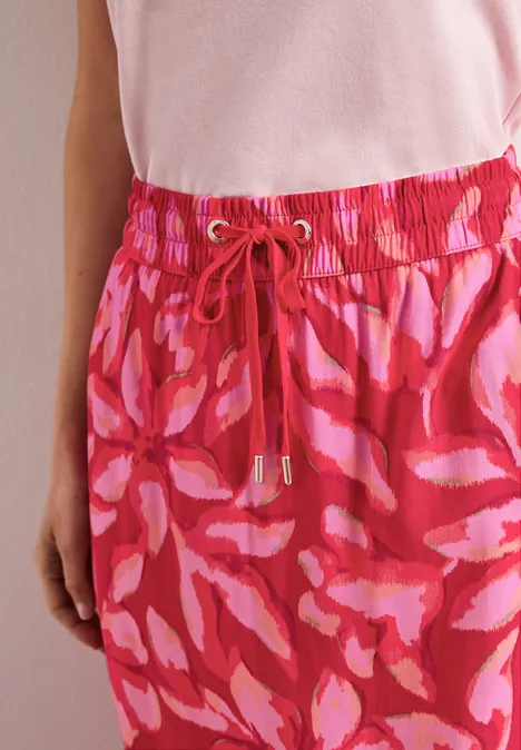 Persoon draagt lichtroze top en loszittende, roze-rode broek met koordtjes in de taille.