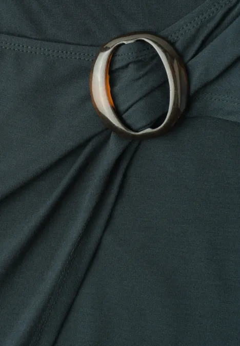 Close-up eines dunkelgrünen Stoffes, zusammengehalten von einem ovalen Ring mit orange-weißer Marmorierung.