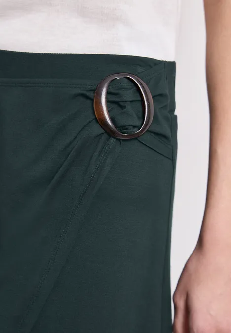 Dunkelgrüner Rock mit großem, runden Gürtelring aus Hornoptik an der Taille.
