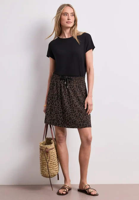 Knielanger Rock mit Elastikbund molten earth Frau in schwarzem Shirt, leopardgemustertem Rock und Sandalen, hält eine Korbtasche vor weißem Hintergrund.