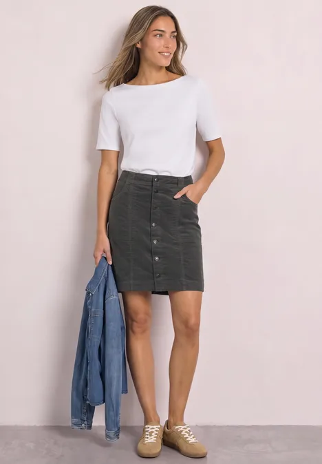 Femme en t-shirt blanc, mini-jupe en velours côtelé vert et baskets, tenant une veste en jean