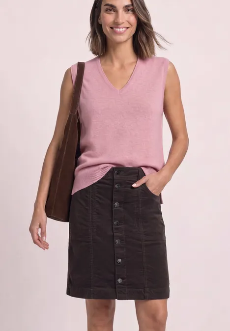 Femme en haut sans manches rose à col V, jupe boutonnée foncée jusqu’aux genoux et sac marron.