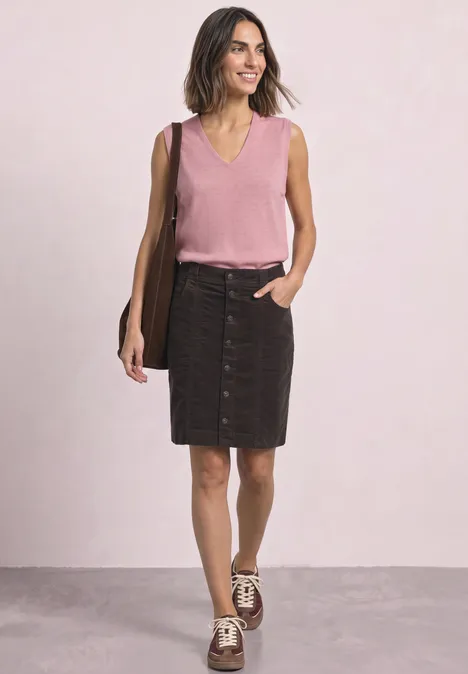 Femme en top sans manches rose et jupe en jean noire boutonnée, sac marron à l'épaule, baskets sur fond clair.