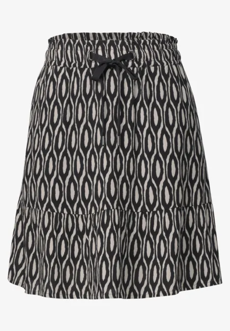 Jupe au genou à imprimé et à volants clay sand Jupe courte noire à motifs blancs organiques, taille élastique et petit nœud décoratif à l’avant.