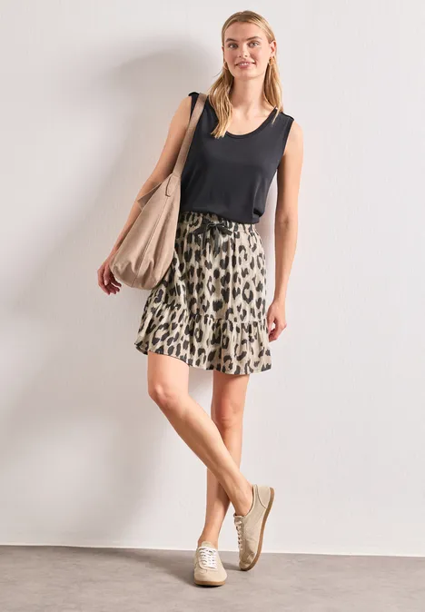 Jupe au genou à imprimé et à volants timeless beige Femme en débardeur noir, jupe léopard, baskets blanches et grand sac devant un mur blanc