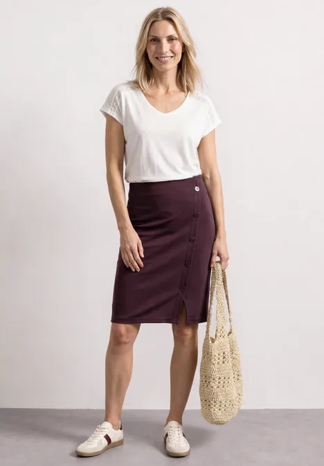 Femme en T-shirt blanc, jupe bordeaux boutonnée, baskets blanches et sac filet