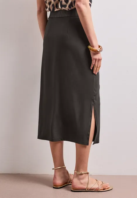 Frau trägt schwarzen Midi-Rock mit seitlichem Schlitz, gemustertem Oberteil und flachen Sandalen.