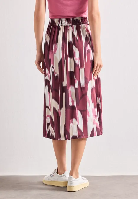 Jupe mi-longue au motif abstrait rose et violet, coupe fluide, portée avec des baskets blanches.