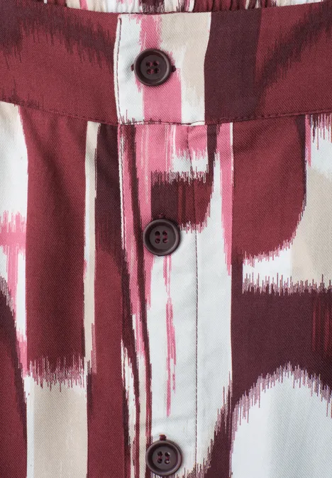 Gros plan d'une chemise à motif abstrait rouge et blanc façon pinceau, ornée de trois boutons foncés.