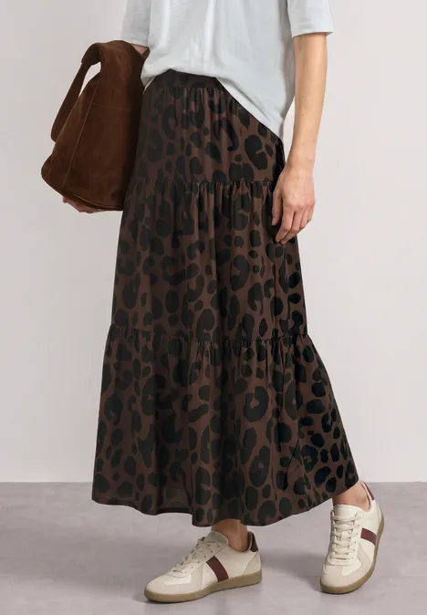 Frau trägt braunen Maxirock mit Leopardenmuster, weiße Sneaker und braune Tasche, weißes Oberteil.