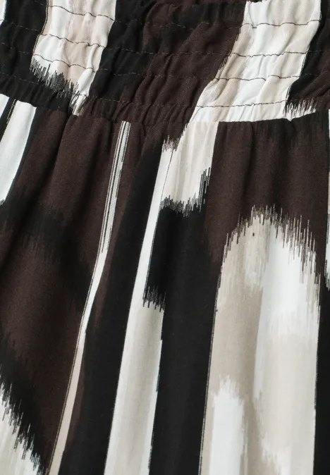 Nahaufnahme eines Stoffes mit elastischem Bund und abstraktem schwarz-weiß-beigem Pinselstrichmuster.