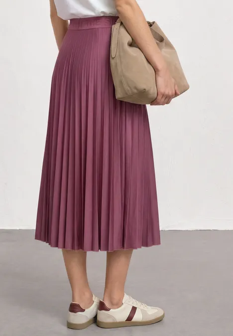 Midirock in Plisséestruktur dark clouded blush Person trägt plissierten, knielangen lila Midi-Rock, weiße Sneaker mit roten Details und eine beige Tasche.