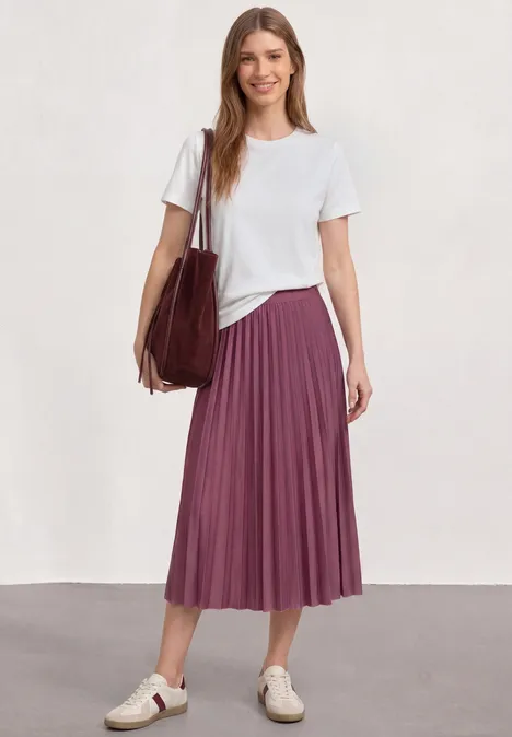 Midirock in Plisséestruktur dark clouded blush Frau in weißem T-Shirt, violettem Plissee-Midirock, weißen Sneakern und großer Handtasche.