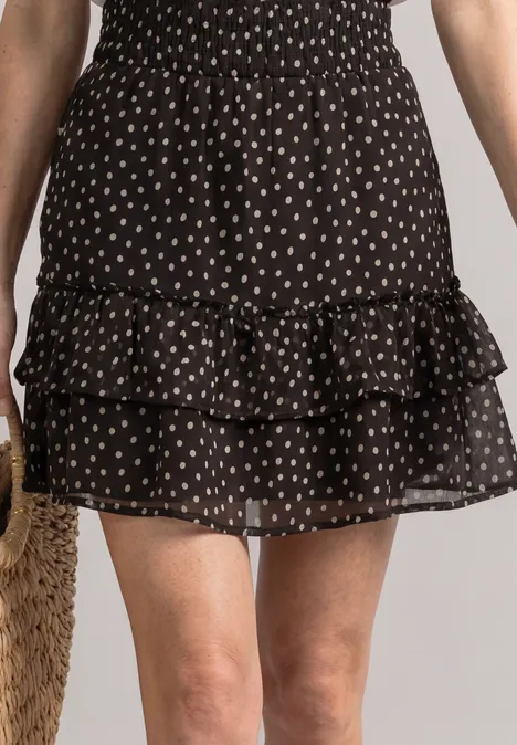 Kniehoge chiffonrok met print black coffee Schwarzer Minirock mit weißen Tupfen und Rüschen, am Körper einer Person.