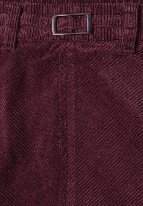 Close-up van een bordeauxrode corduroy broek met riem en fijn ribpatroon