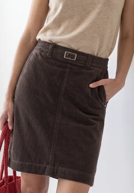 Donkerbruine ribfluwelen rok met riem, zijzak, licht topje en rode handtas.