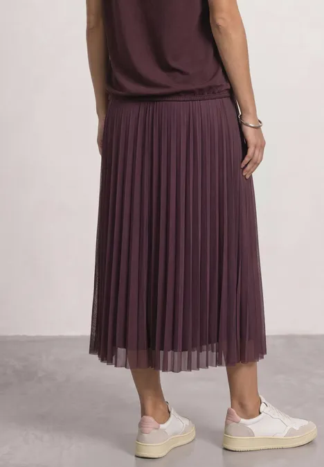 Midirok van mesh met plissé-structuur rustic rouge Frau von hinten in dunkelviolettem, plissiertem Midirock und weißen Sneakern vor neutralem Hintergrund.