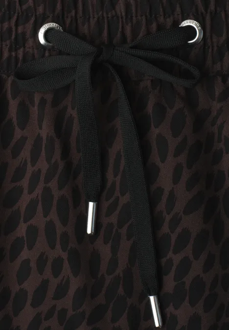 Jupe mi-longue à taille élastiquée et fentes molten earth Gros plan sur un cordon noir à embouts métalliques sur un tissu marron à motifs.