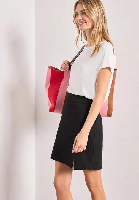 Frau mit weißem T-Shirt und schwarzem Rock trägt rote Tasche über der Schulter.