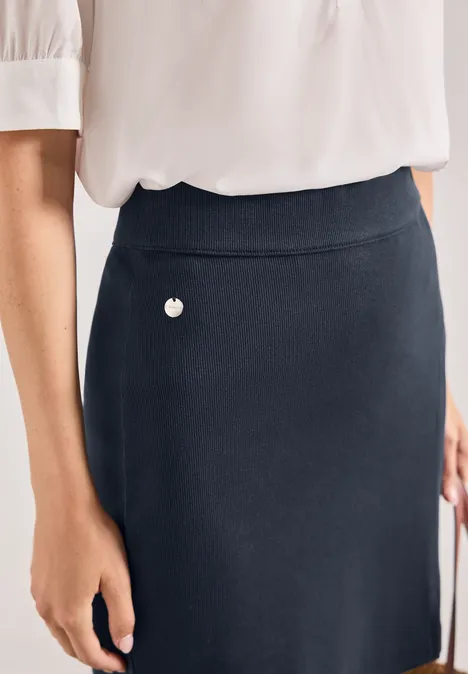 Femme portant un chemisier blanc et une jupe bleu marine ornée d’un petit cœur.
