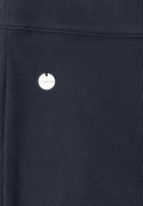Gros plan sur un tissu côtelé bleu foncé avec une petite pastille ronde blanche à logo.