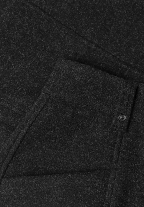 Zwarte stof met opgestikte zak, schuine opening en knoopdetail.