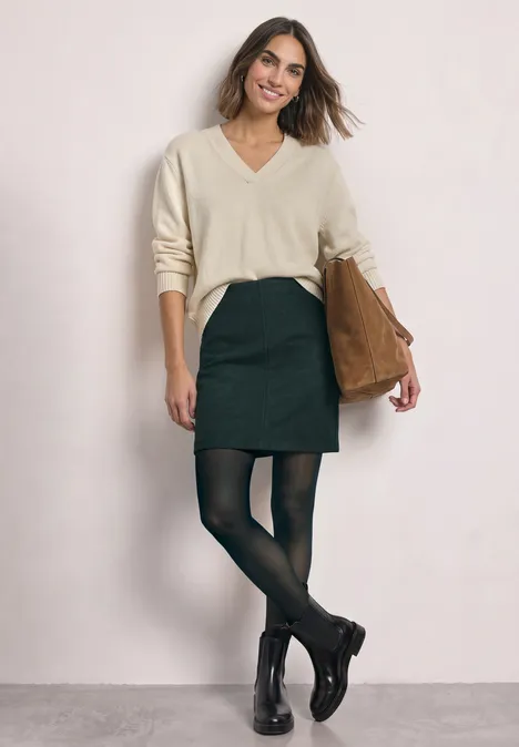 Knielanger Rock in Wolloptik stormy green Eine Frau in beigem V-Pullover, schwarzem Rock, schwarzen Strumpfhosen und Stiefeletten mit brauner Tasche.