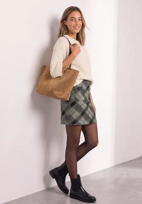 Knielanger Rock mit Patch-Pockets sanded amber Frau in beigem Pullover, kariertem Rock, schwarzen Strumpfhosen und Boots trägt braune Tasche vor weißer Wand.