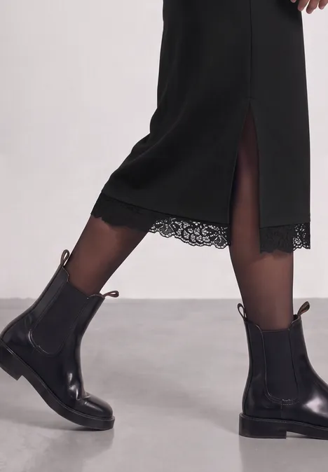 Schwarzes Midikleid mit Spitzensaum und schwarze Chelsea-Stiefel.
