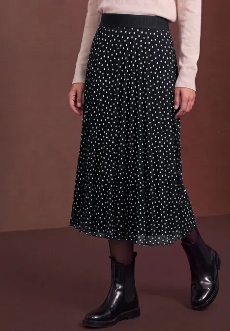 Jupe midi noire à pois blancs, associée à un haut crème et des bottines noires.