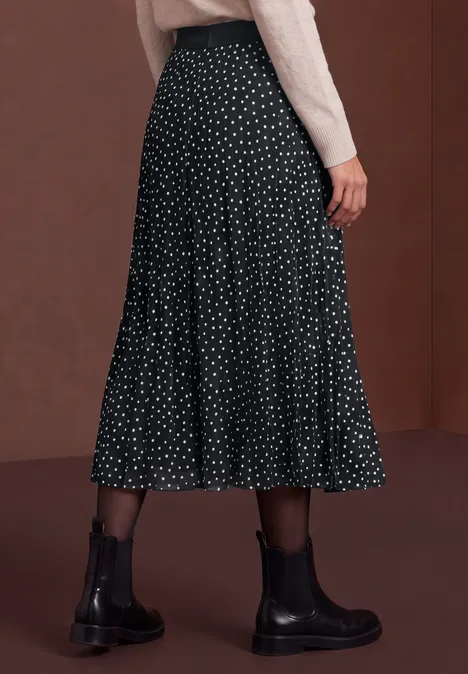 Jupe midi noire à pois blancs, portée avec des bottines noires.