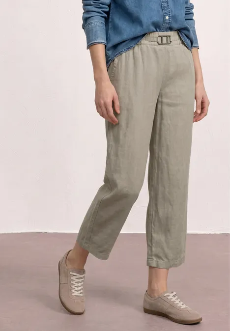 Linnenbroek in olijfgroen met riem, losvallend tot op de enkels, gecombineerd met beige sneakers.