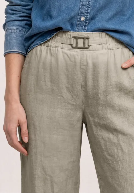 Close-up van persoon in beige linnenbroek met riem en blauw denim overhemd, hand bij de taille