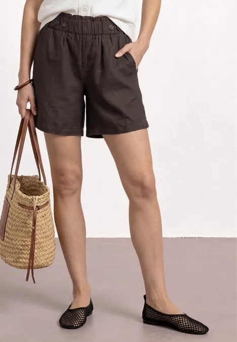 Eine helle Bluse, lockere schwarze Shorts, eine Strohtasche und schwarze Netzballerinas.