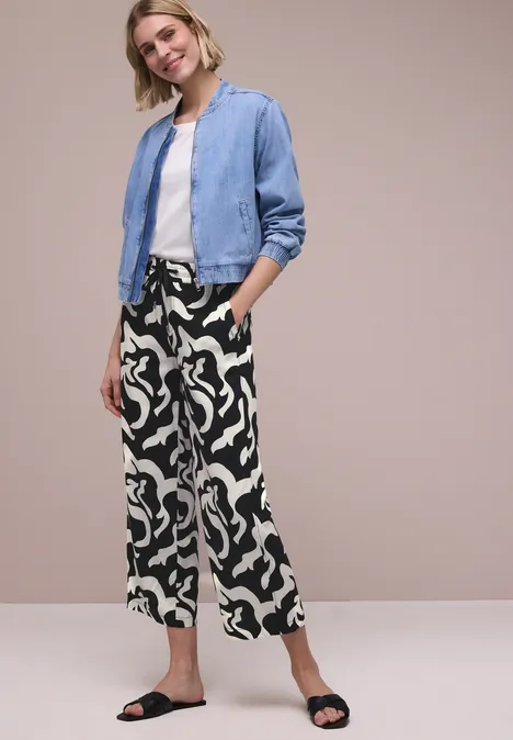 Modieuze vrouw in blauwe bomberjack, wit t-shirt, zwart-witte culottes en zwarte sandalen.