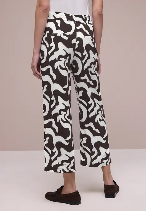 Achteraanzicht van een persoon in wijde broek met zwart-wit abstract patroon en zwarte pantoffels.